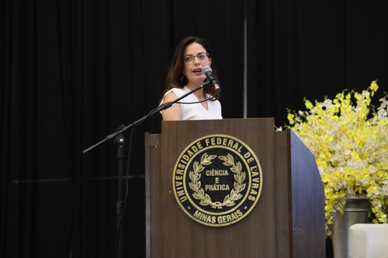 Dra. Gerusa Vilas-Bôas falando atrás do púlpito de um auditório universitário.